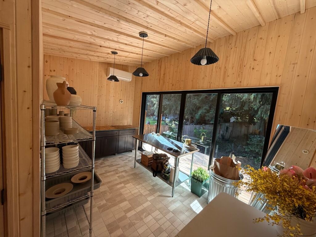 Wood-lined backyard studio interior with pendant lights and a worktable